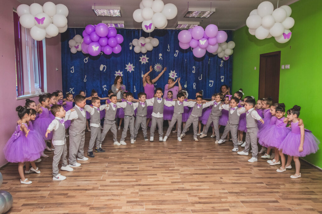 ბავშვთა საცეკვაო ანსამბლის გამოსვლა სცენაზე იასამნისფერი დეკორაციებით.